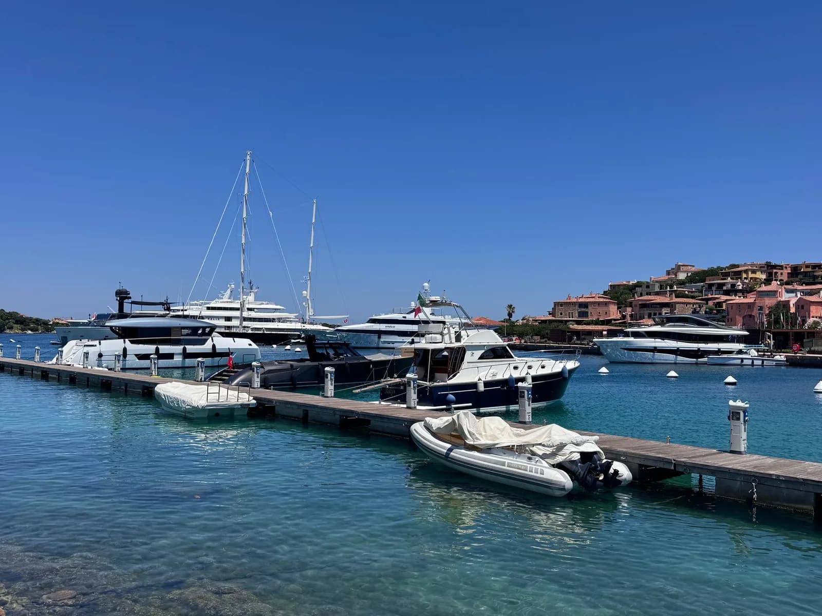 Yachts amarrés dans la marina de Porto Cervo, maisons ocre du village sur la colline